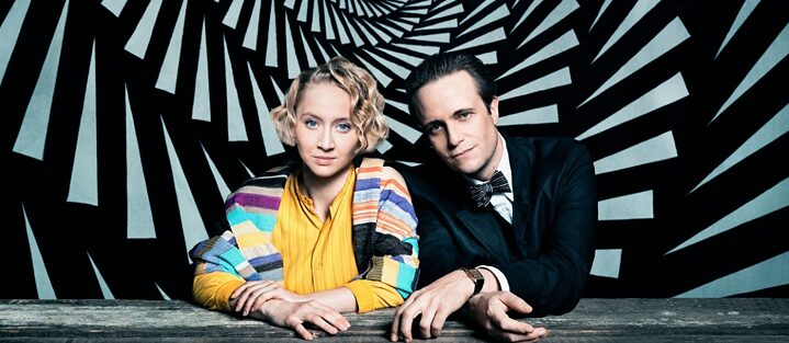 Werbemotiv aus der Serie „Die neue Zeit“: Anna Maria Mühe als Dörte Helm und August Diehl als Walter Gropius vor einem gemalten Spiralwirbel. 