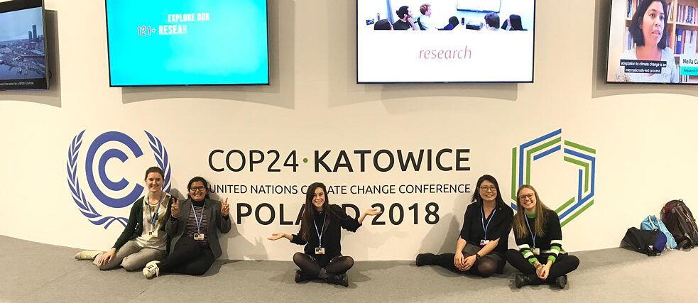 Auf der COP24 Fünf junge Aktivistinnen posieren vor dem Gipfel-Logo. Über ihnen sind Bildschirme zu sehen.