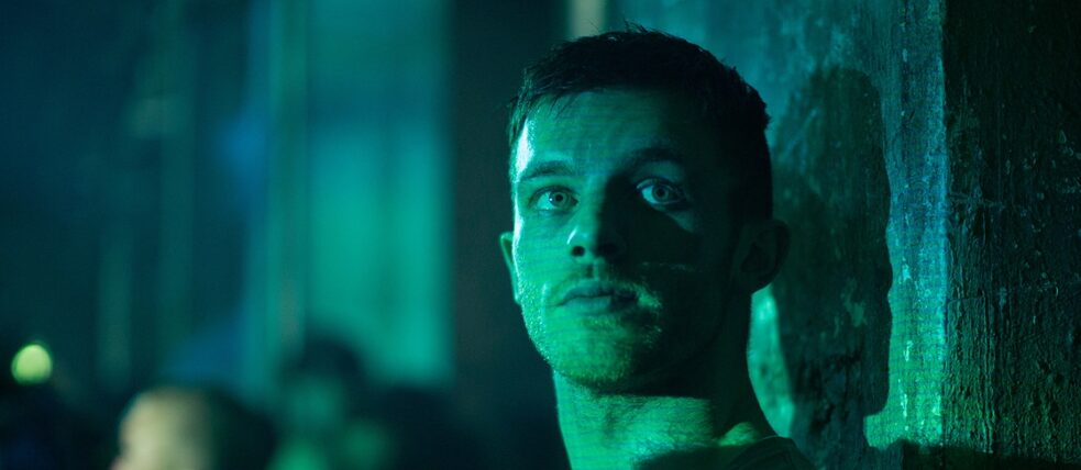 Still frame from the Amazon Prime series “Beat”: the club promoter “Beat” ( Jannis Niewöhner) leans against a concrete pillar, the room and his face are bathed in green light.