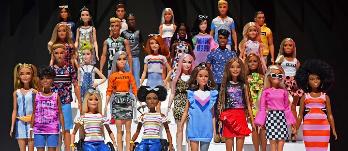 Viele diverse Spielzeugbarbies vor schwarzem Hintergrund