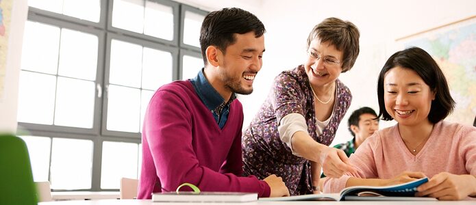 A smiling teacher supports three adult language students.