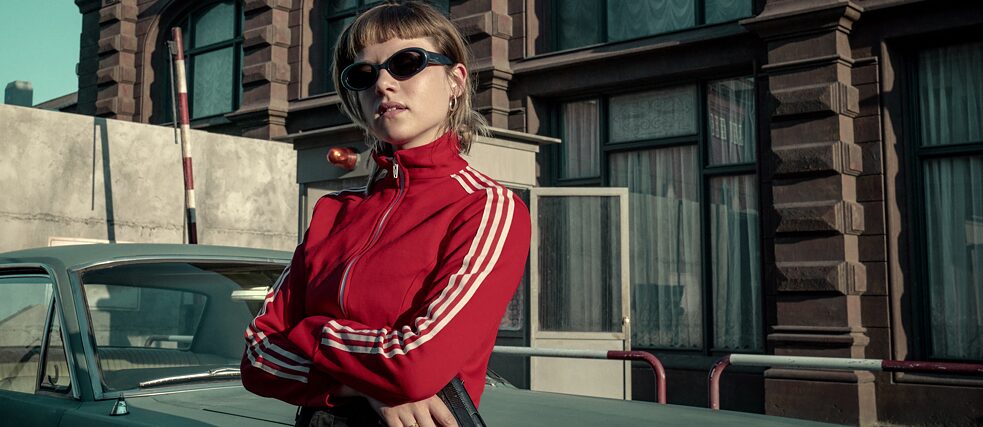 Kleo Titelbild aus der Netflix-Originalserie "Kleo" zeigt die Titelfigur dargestellt von Jella Haase in einer roter Trainingsjacke mit einer Pistole in der Hand