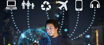 Mann mit Handy vor einem Hologramm einer Weltkugel im Hintergrund befinden sich verschiedene Symbole wie ein Flugzeug oder ein Computer.