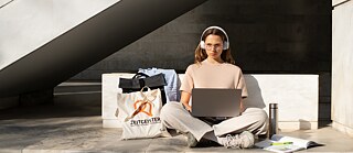 Frau sitzt draußen mit Laptop