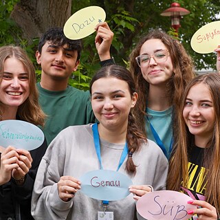 PASCH-Schüler*innen lächeln in die Kamera und halten bunte Zettel mit deutschen Wörtern nach oben.