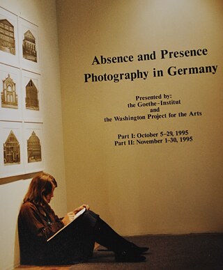 In a gallery, a young woman sits on the floor