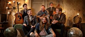 Les membres du groupe Versengold, six hommes sont assis sur un canapé et sourient à la camera.
