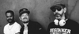 Die drei Musiker grinsend vor einer Wand
