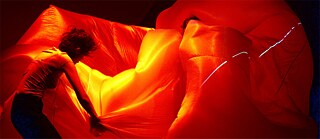 Tänzerinnen mit rot-gelb angestrahlter Blase aus Stoff