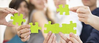 Hände halten grüne Puzzle-Teile in die Kamera