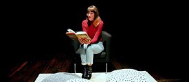 Deborah Weber liest ein Buch, während sie auf einem Stuhl sitzt. Vor ihr werden Kissen auf den Boden gelegt.