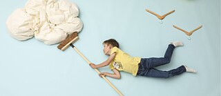 Fotoinstallation eines Jungen der mit Vögeln in der Luft schwebt und eine Wolke mit einem Besen wegschiebt.