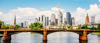 View of Ignatz Bubis Bridge, with the skyline of Frankfurt am Main in the background. Blue sky, sun and clouds.