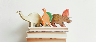 Auf einem Bücherstapel stehen drei bunte Spielzeug-Dinosaurier aus Holz