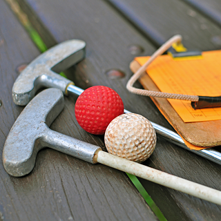 Miniature golf clubs and balls and a small clipboard with a yellow score card.