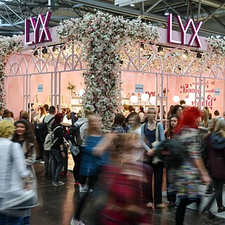 Zahlreiche Menschen passieren den zartrosanen Stand von LYX auf der Leipziger Buchmesse 2025.