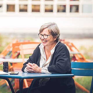Auf dem Foto sieht man wie Jenny Erpenbeck lächelnd im Garten dem Journalisten gegenübersitzt