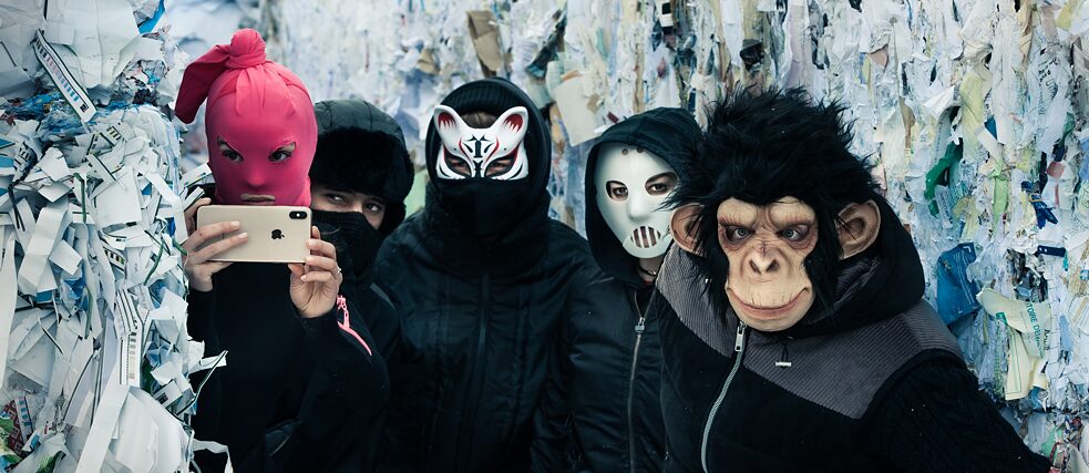 Still frame from the Netflix Series "We Are The Wave" - Five masked persons hiding between bales of reclaimed paper